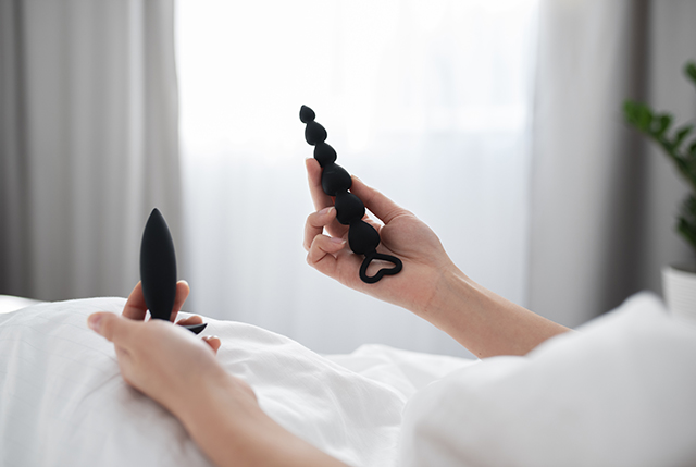 person in bed holding two anal vibrators